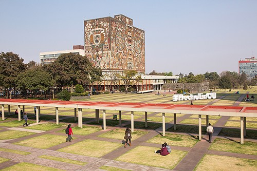 The Central Library building covered with a decorative mural by Juan O'Gorman, with a plaza and green lawn in front.