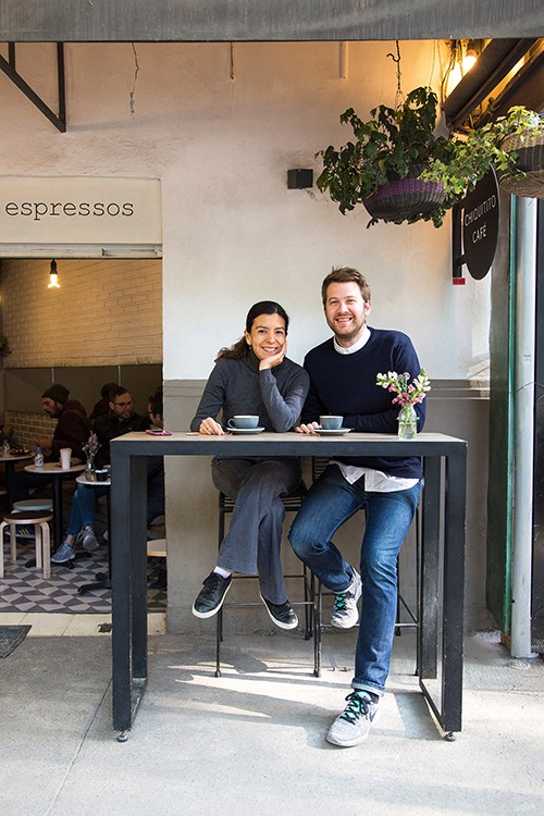 Two people sitting at a high table outside Chiquitito Café with espresso signage visible behind them.