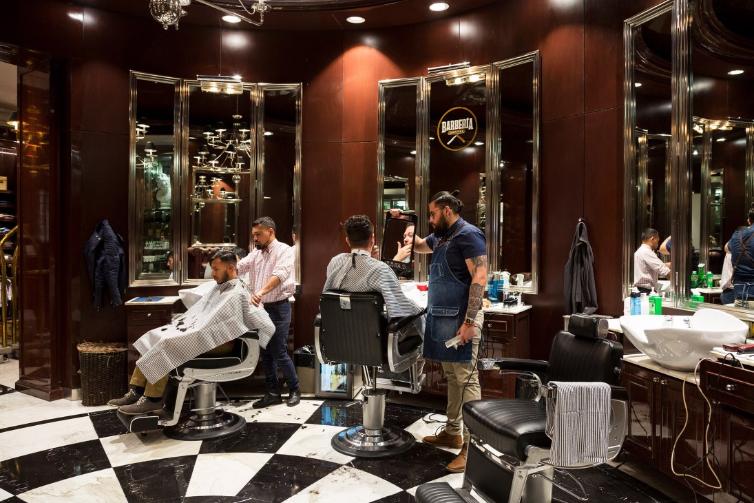 Barbería Capital barbershop interior with barbers working on customers at vintage-style stations with large mirrors.