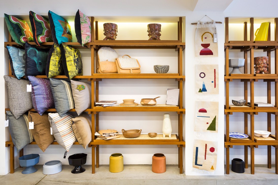 Wooden shelves displaying colorful Mexican crafts including pillows, ceramics, baskets and home goods at Ikal shop.