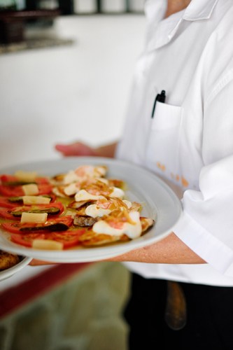 Chef in white chef's coat holding plate of Spanish seafood tapas including fried anchovies and other coastal dishes.