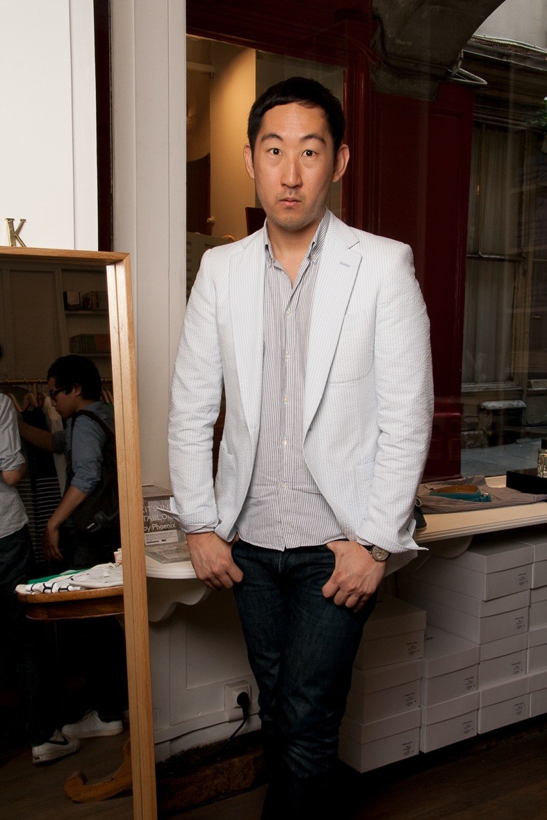 Man in light grey blazer and striped shirt standing in modern retail interior with wooden fixtures.