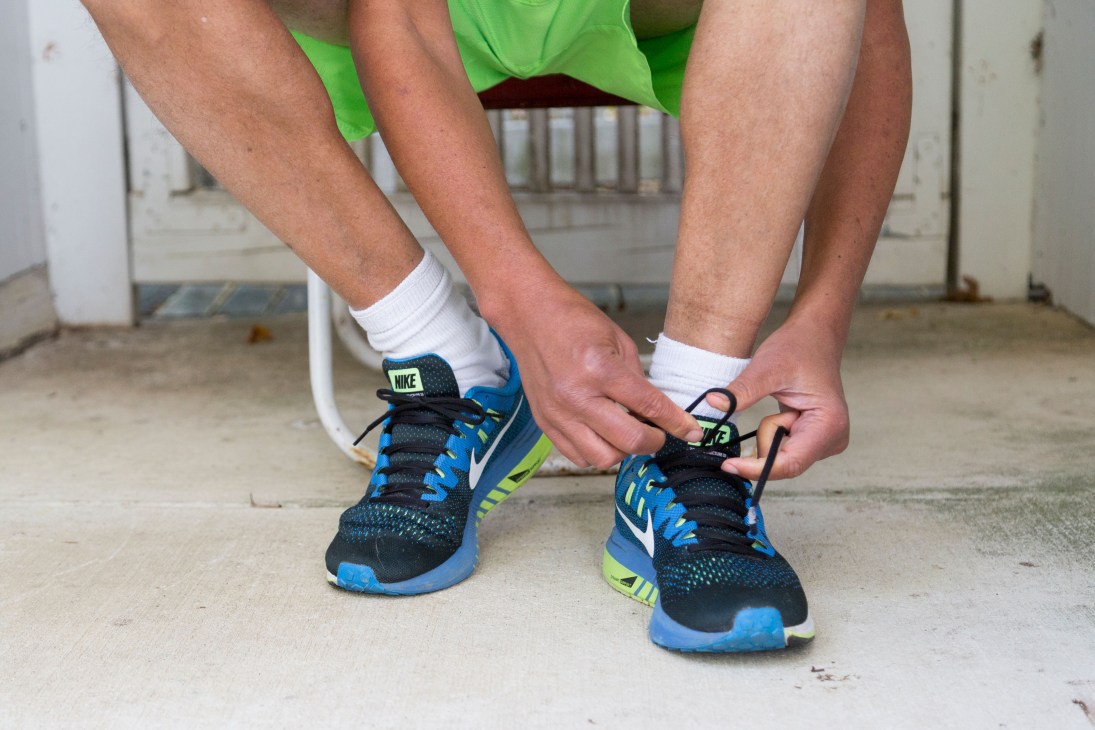 Person tying Nike running shoes while wearing white socks and green shorts.