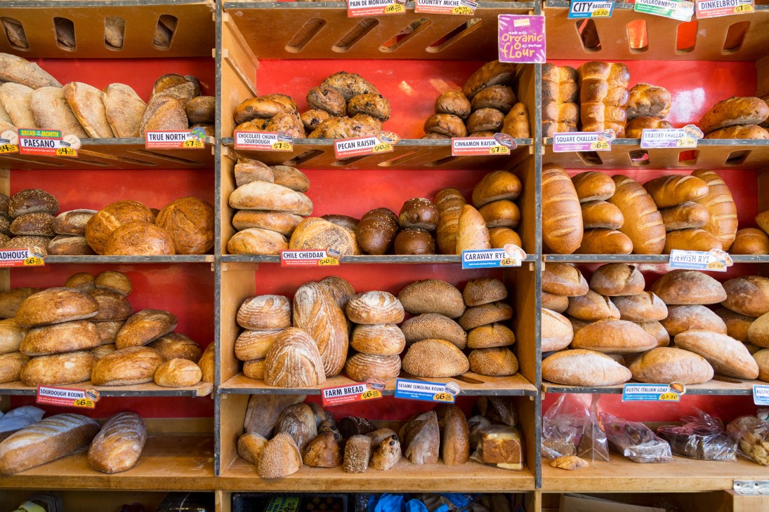 Display shelves of various artisanal breads with labeled price cards at Zingerman's bakery.