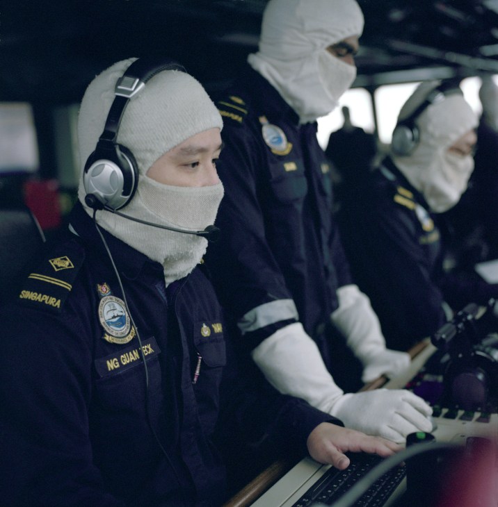 Singapore Navy personnel in cold-weather gear operating equipment on a ship bridge.