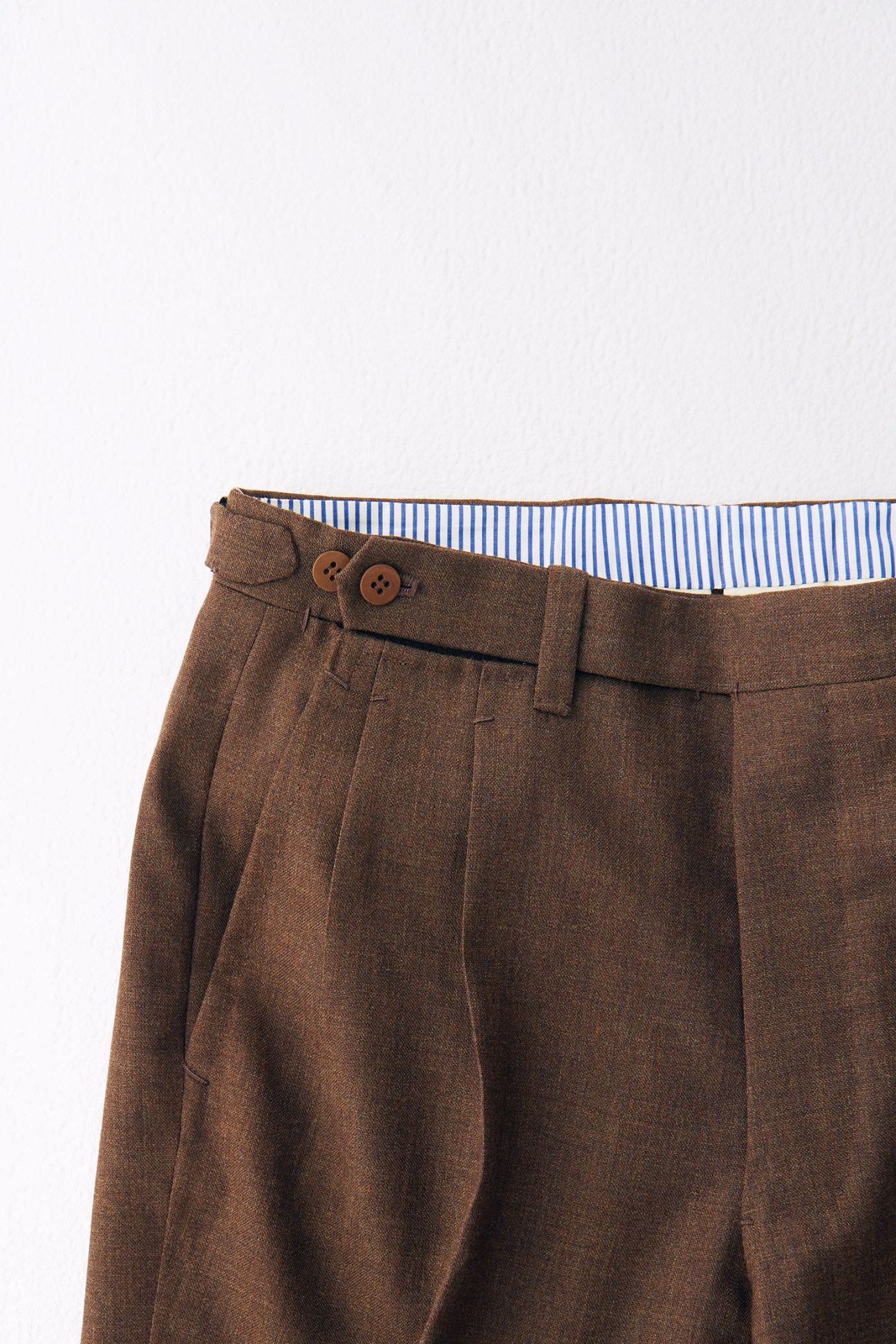 Brown wool trousers with pleated front and blue striped shirt detail at waistband.