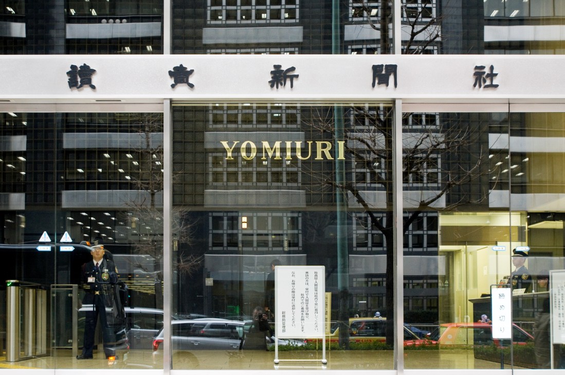 Yomiuri Shimbun headquarters building entrance in Otemachi, Tokyo, with Japanese characters and gold lettering on glass facade.