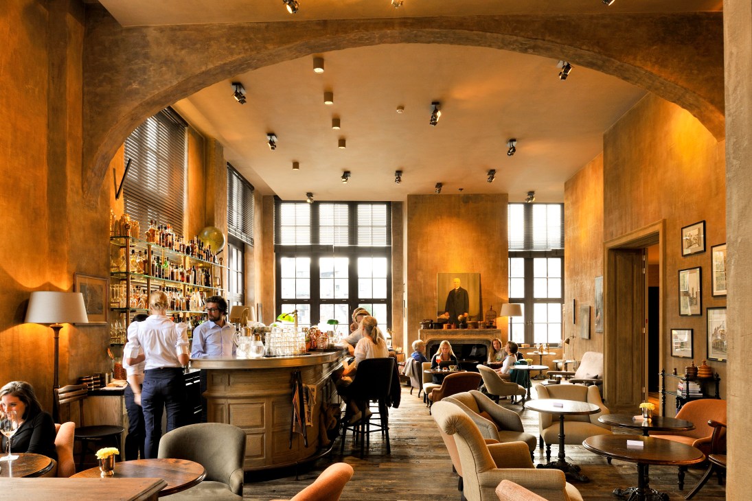Interior of 1898 The Post hotel bar and kitchen in Ghent with warm amber lighting and wooden furnishings.