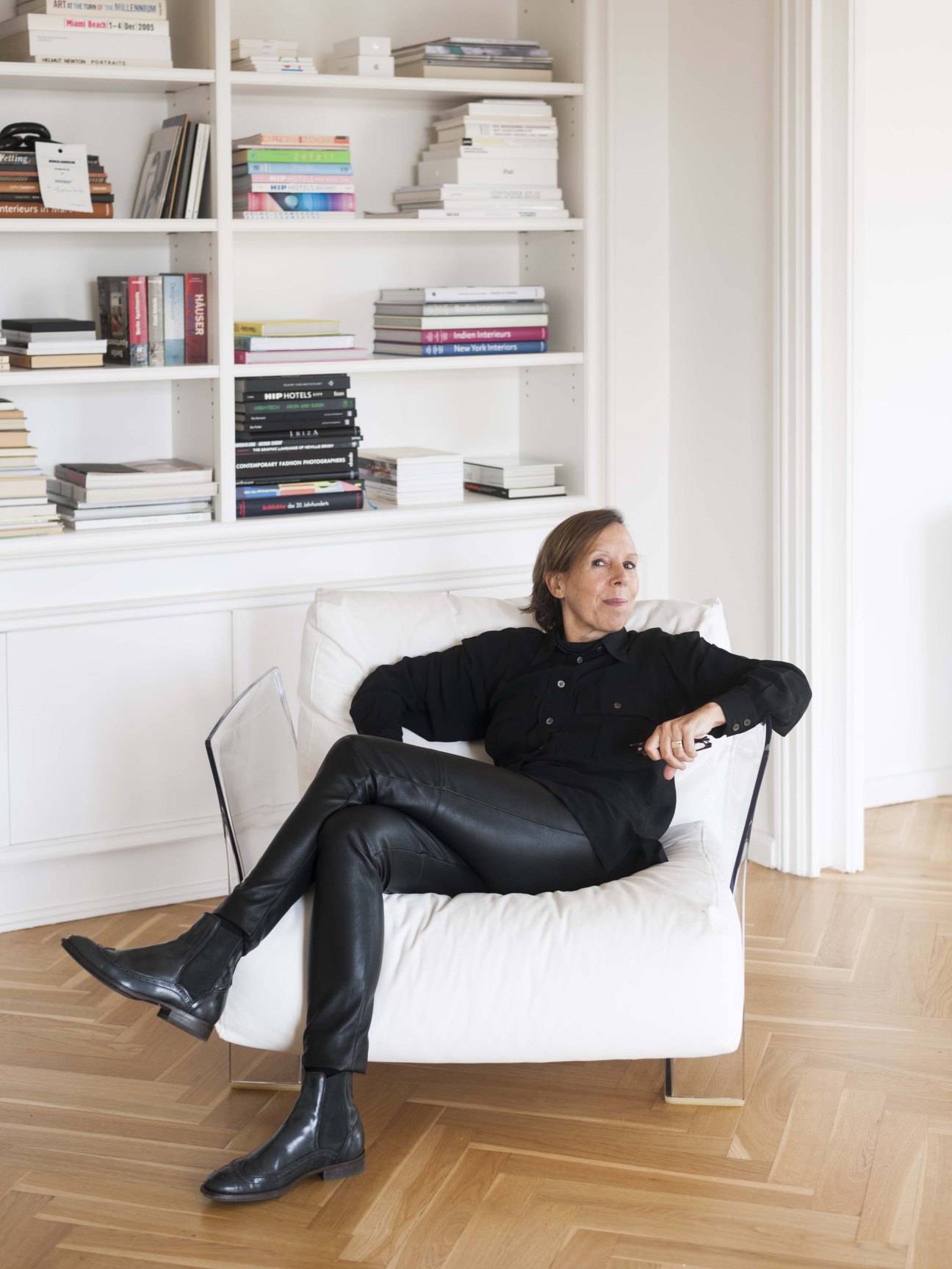 Eva-Maria Steidel sits in a minimalist white chair against built-in bookshelves in the Henselmann Tower apartment.