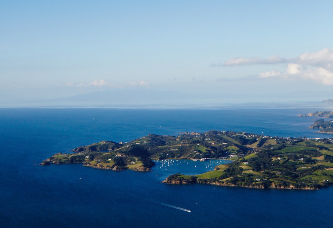 Aerial view of islands in the Hauraki Gulf with green hillsides, moored sailboats, and blue water surrounding New Zealand.