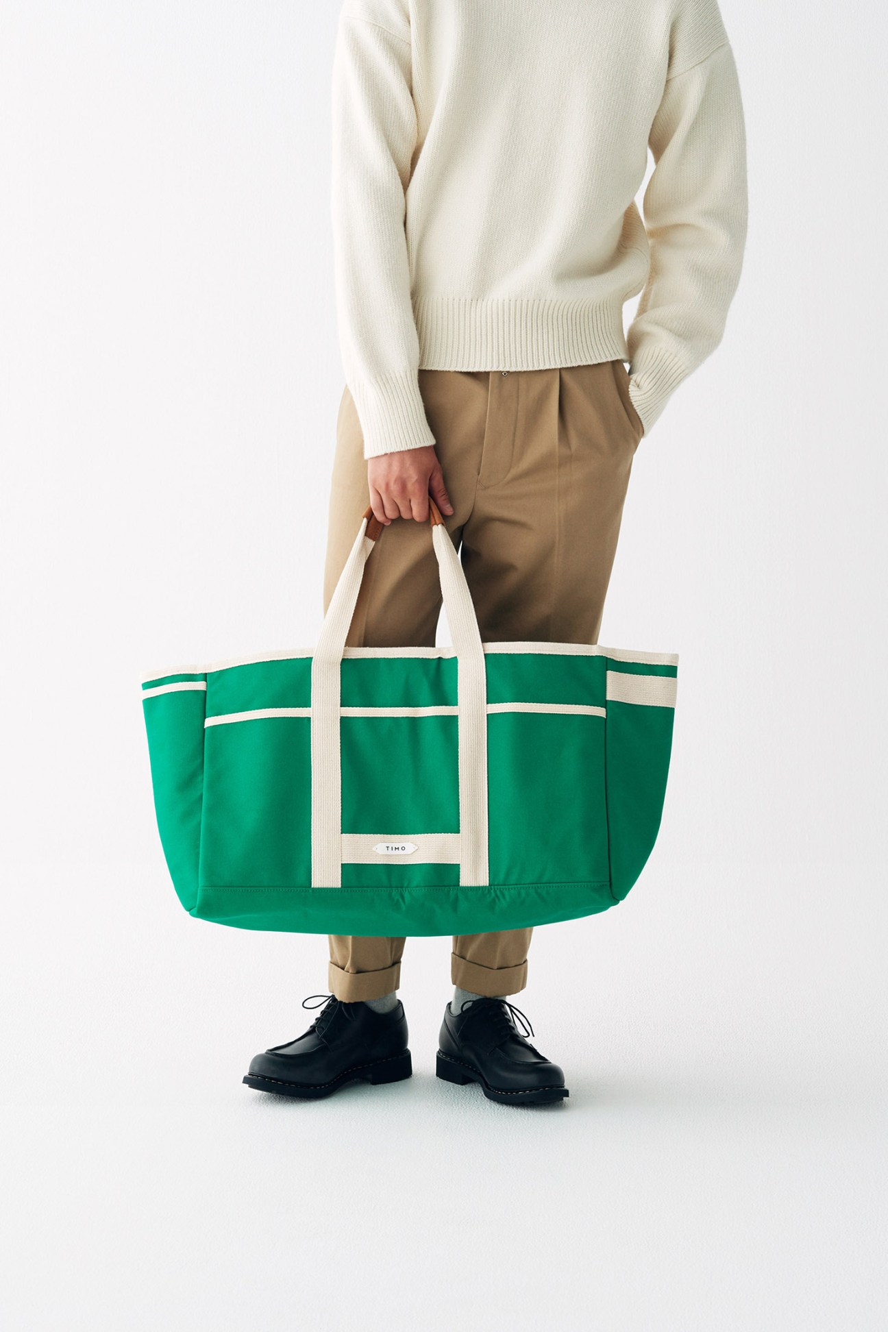 Person holding a green canvas tote bag with white straps and TIMO branding.