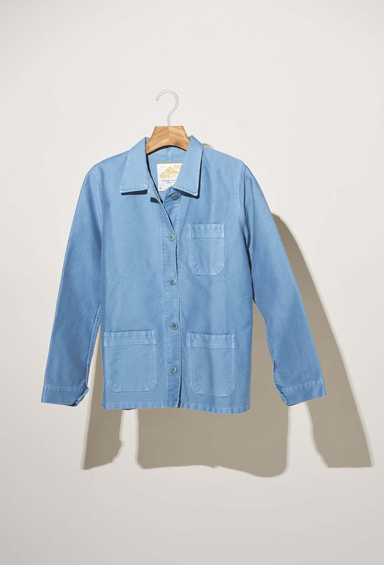Light blue denim work jacket on wooden hanger against white background