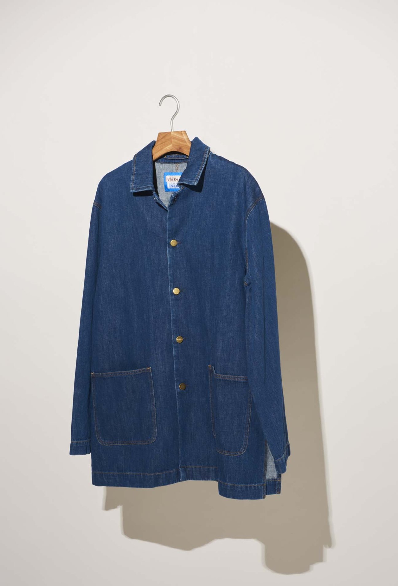 Blue denim jacket on wooden hanger against white background