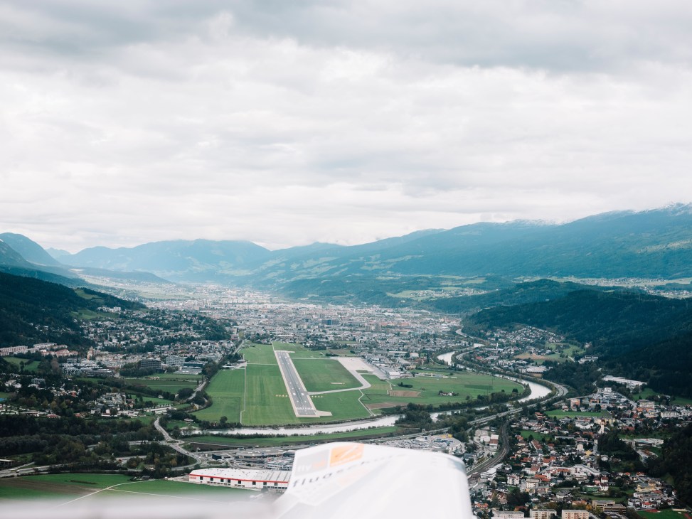 Aerial view of an aircraft approaching Innsbruck Airport with snow-capped Alpine peaks surrounding the runway.
