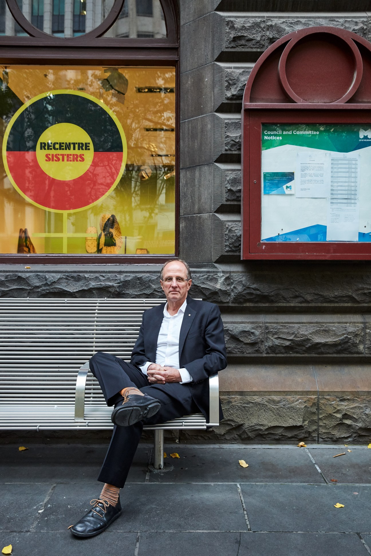 Rob Adams sitting on a bench in front of a building with a colorful Recentre Sisters sign.