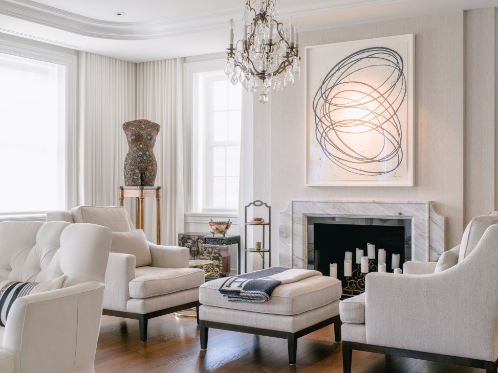 Elegant living room with cream upholstered chairs, marble fireplace, crystal chandelier, and abstract artwork in the Beckers' Chateau apartment.