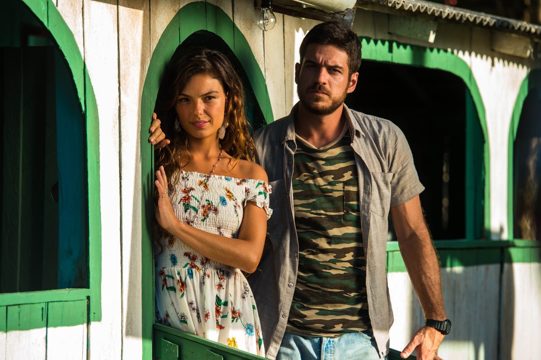 A woman and man stand together in front of bright green doors, illustrating Brazilian television's cultural presence.