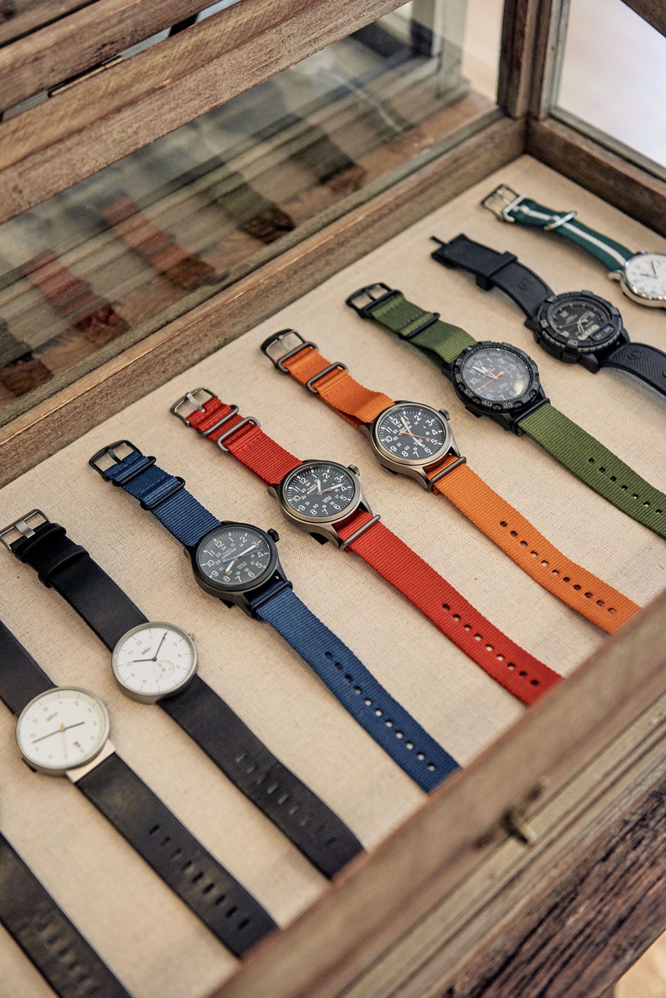 Collection of watches with various colored fabric straps displayed in a wooden drawer.
