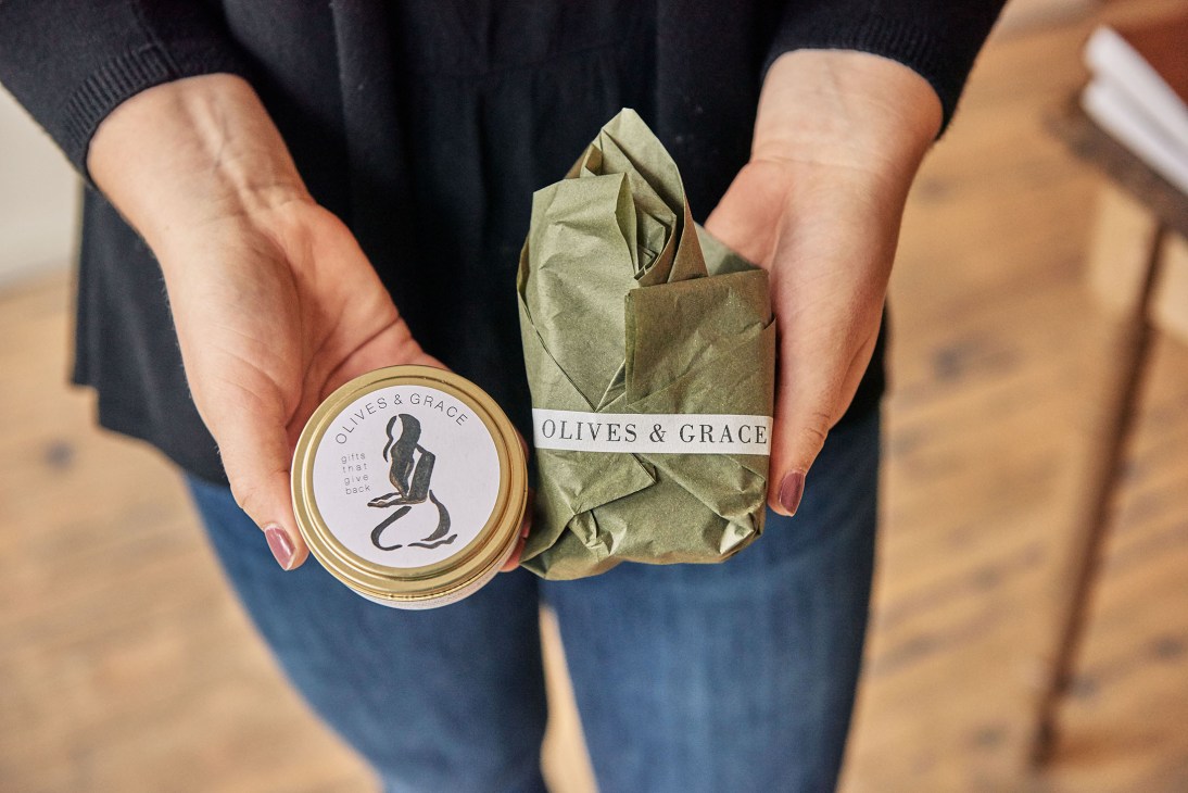 Hands holding Olives & Grace gift box and kraft paper wrapped product with brand label.