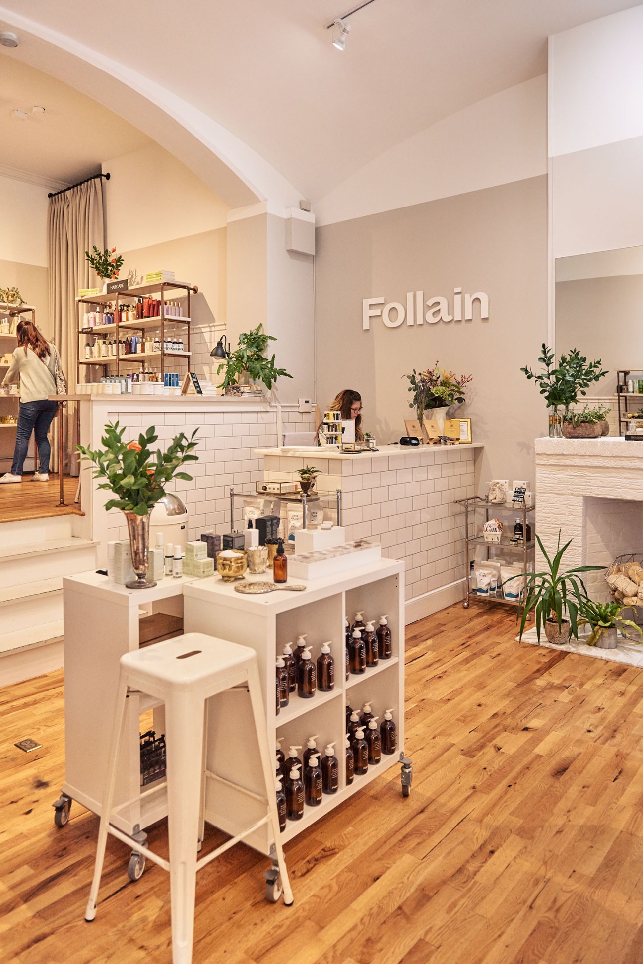 Interior of Follain beauty shop with white subway tile, wooden floors, product displays, and green plants throughout.