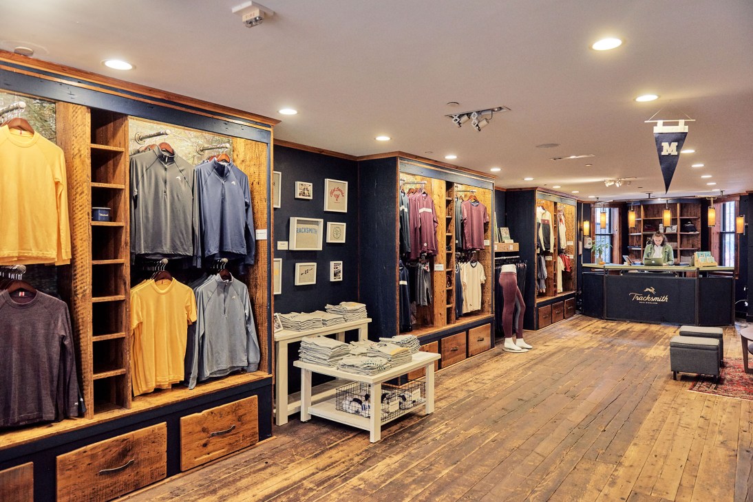 The Tracksmith retail store interior on Newbury Street with wooden display fixtures, clothing racks, and a checkout counter.