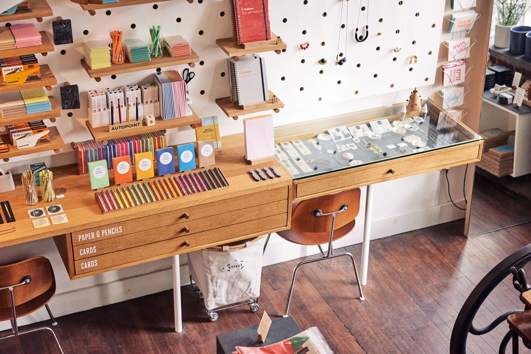 Interior of Loyal Supply Co with wooden pegboard wall, stationery displays, colored pencils, and printing press in Boston shop.