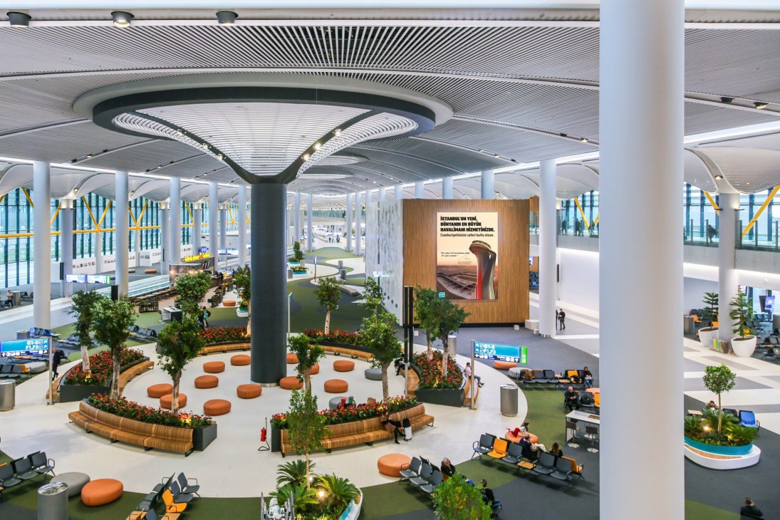 Istanbul's new airport terminal featuring modern architecture with curved ceiling, green landscaping, orange seating, and natural light from large windows.