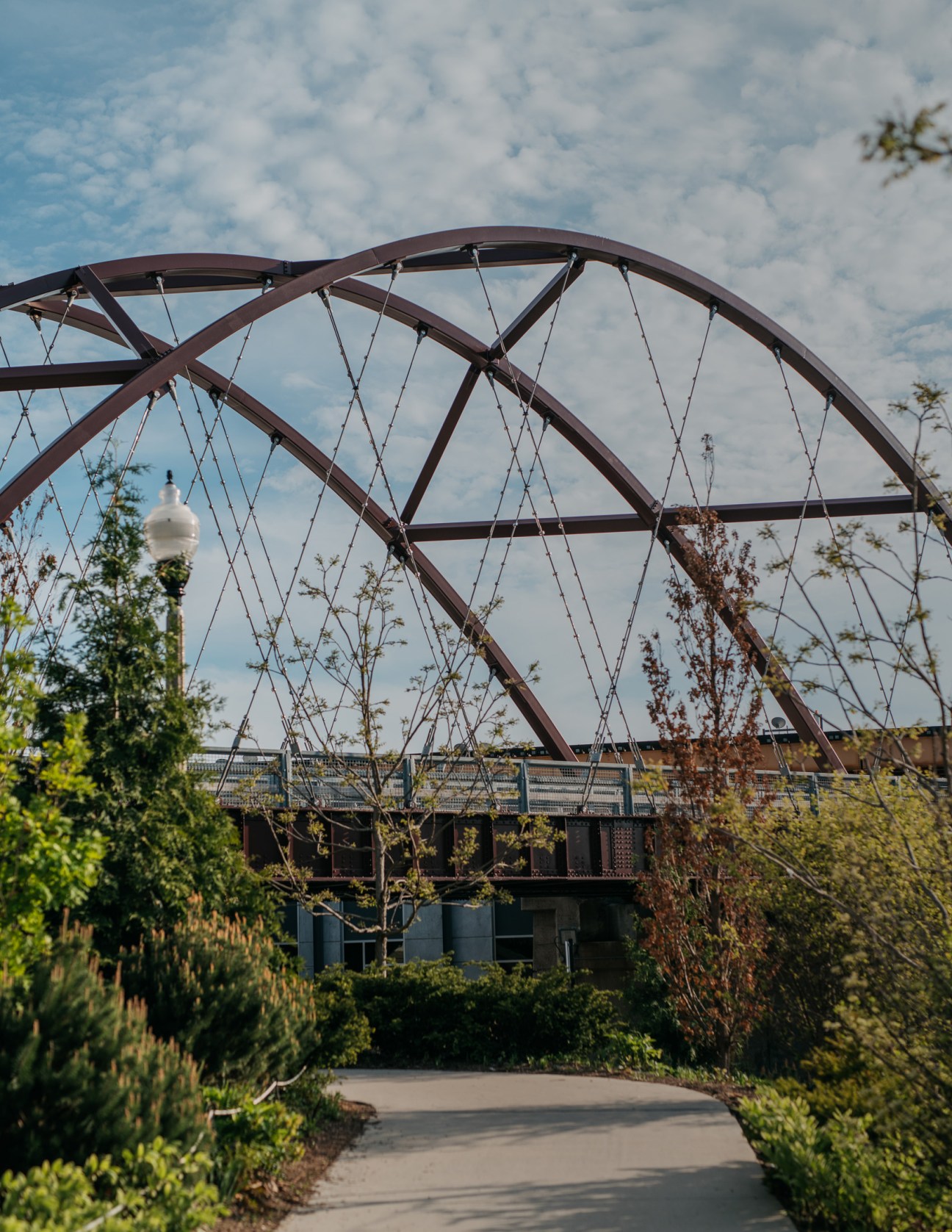 Arched steel bridge structure over The 606 elevated park with vegetation and cloudy sky.