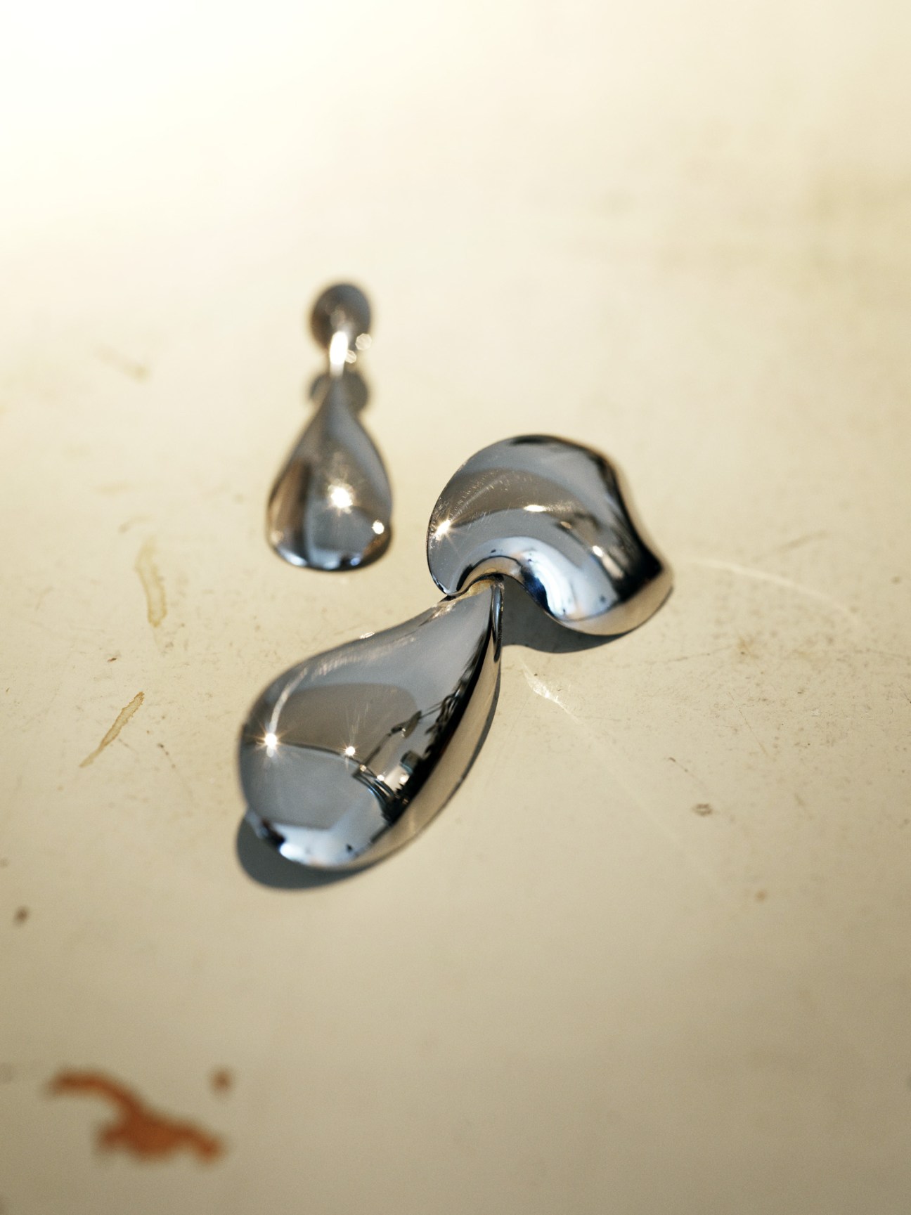 Two polished chrome teardrop-shaped earrings displayed on a light textured surface.