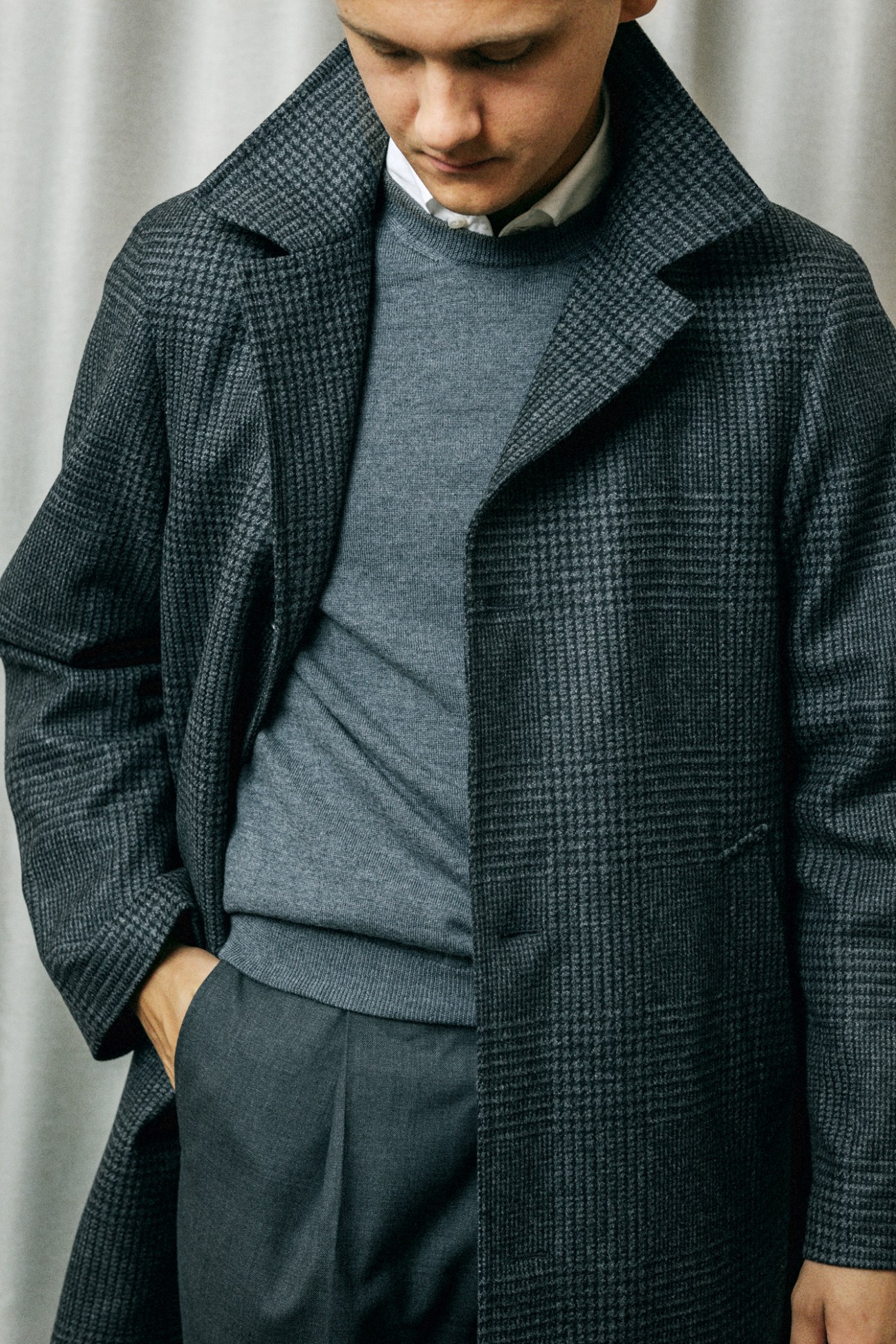 Man wearing dark grey overcoat with split-Raglan sleeves and popped collar over casual clothing.
