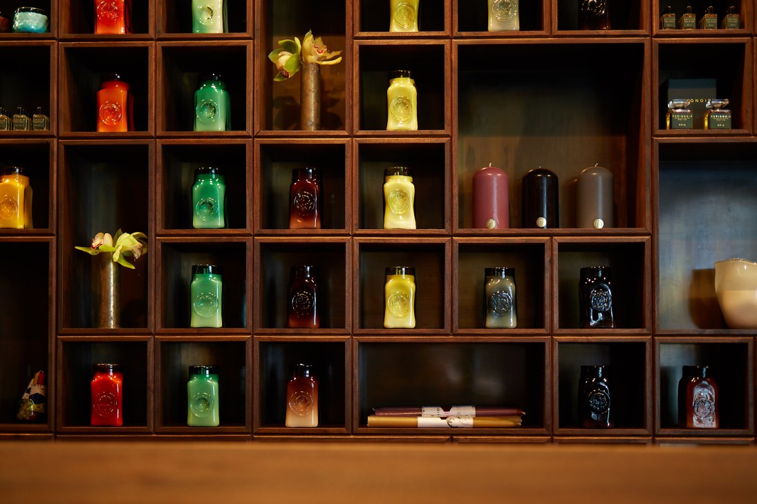 Wooden shelving unit displaying colorful illuminated fragrance bottles and handmade candles at Curionoir perfume shop.