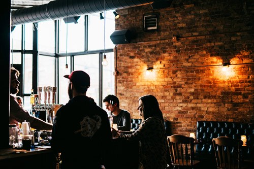 Interior of Blind Barber barbershop and speakeasy with customers at the bar and exposed brick walls.