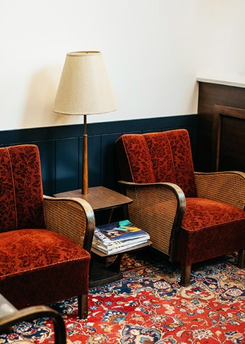 Interior seating area at The Publishing House B&B with red patterned armchairs, table lamp, and magazines.
