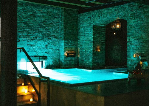 Glowing turquoise thermal bath at Aire Ancient Baths in Chicago with brick walls and ambient lighting.