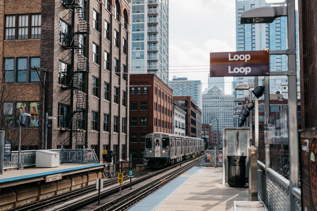 Chicago L train platform with elevated tracks, Loop station sign, and city skyline in background.