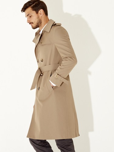 Man wearing a beige trench coat over dark trousers, photographed in profile against a white background.
