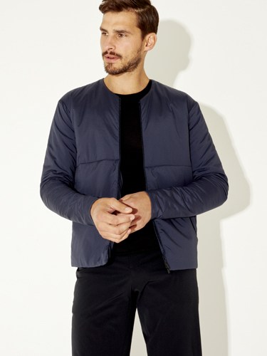 Man wearing navy quilted jacket and black shirt against white background