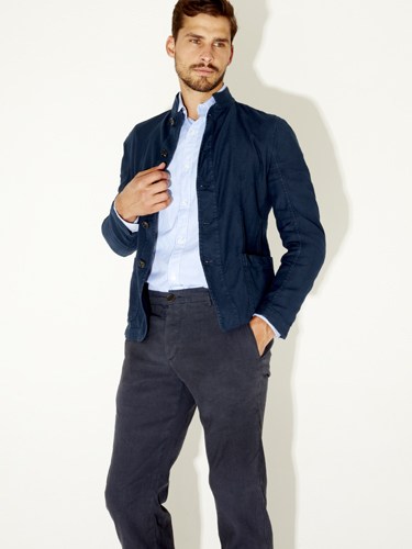 Man wearing navy quilted jacket, light blue shirt, and dark trousers against white background.