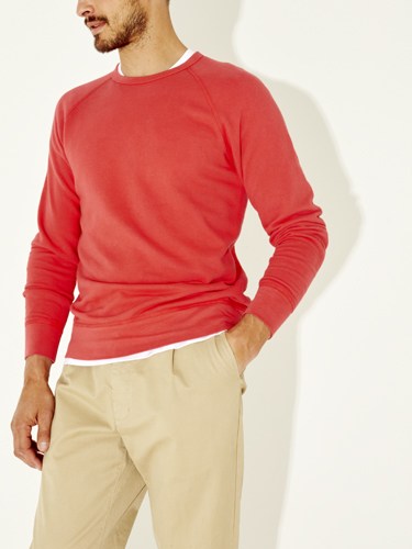 Man wearing a red raglan sweatshirt and beige trousers against a white background.