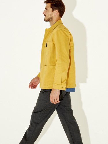 Man wearing bright yellow jacket with blue lining over dark trousers, shown in profile against white background.