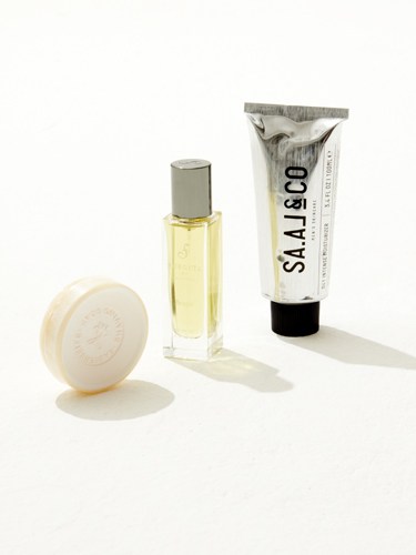 Three sustainable grooming products: a white soap bar, yellow cologne bottle, and white skincare tube labeled Saal & Co.