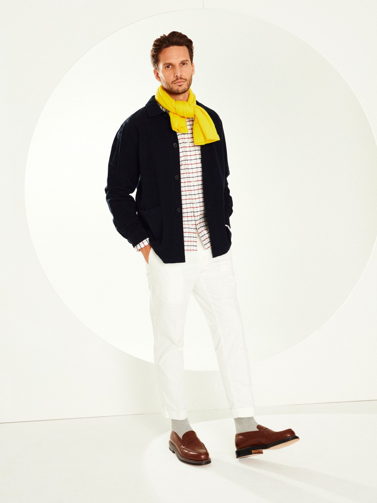 Man wearing black blazer, yellow scarf, checkered shirt, white trousers, and brown loafers.