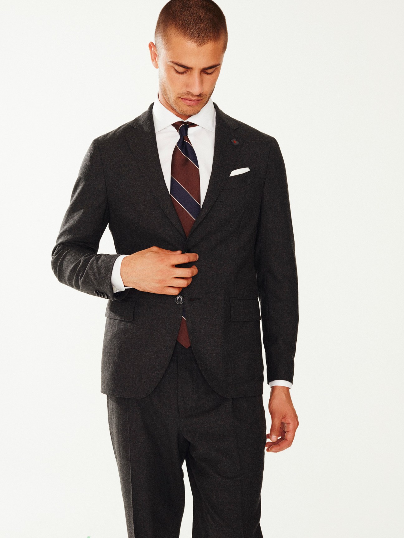 Man wearing charcoal suit, white dress shirt, and striped tie looking downward.