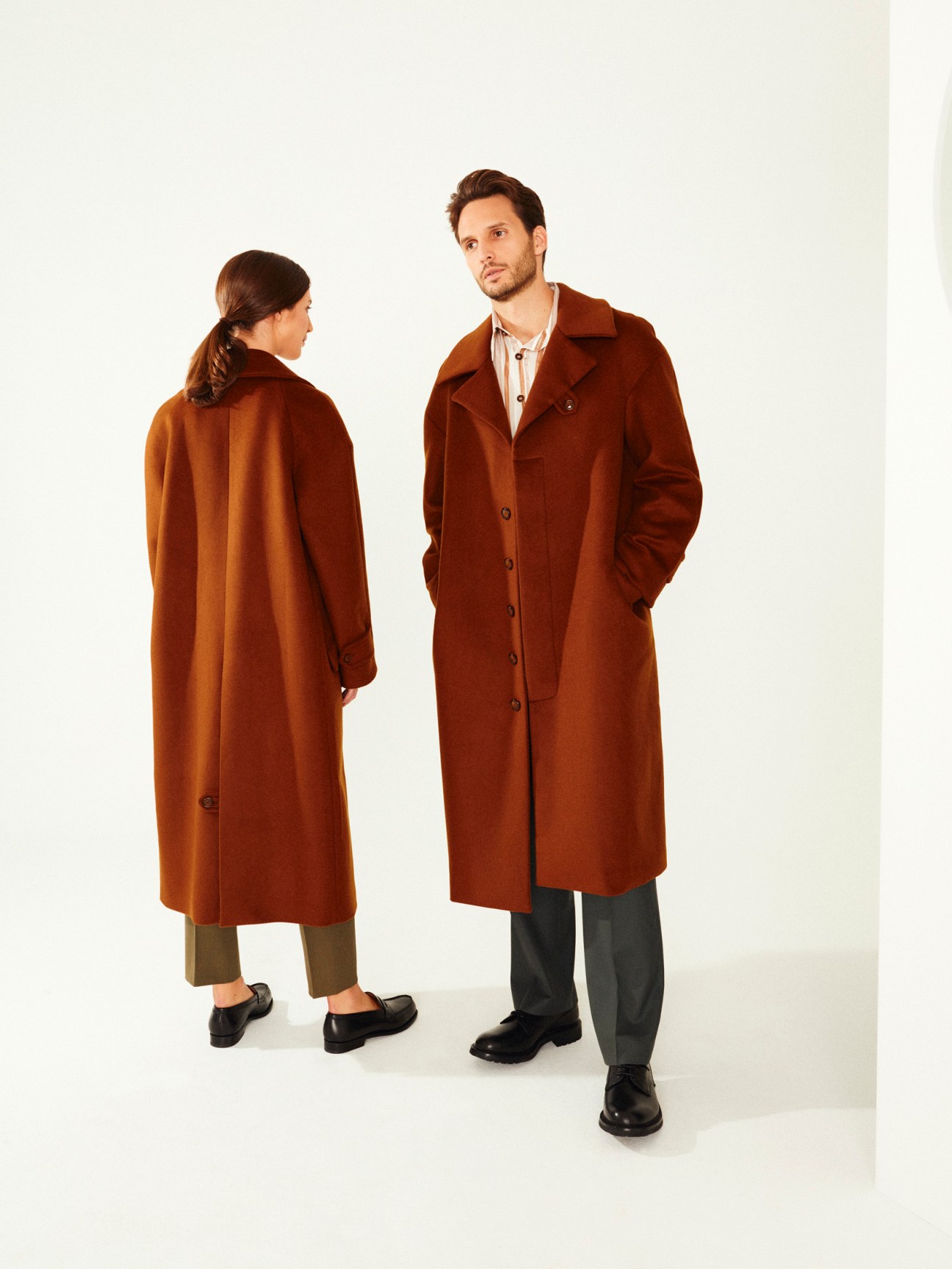 Two models wearing rust-colored wool coats with collared shirts, styled for autumn.
