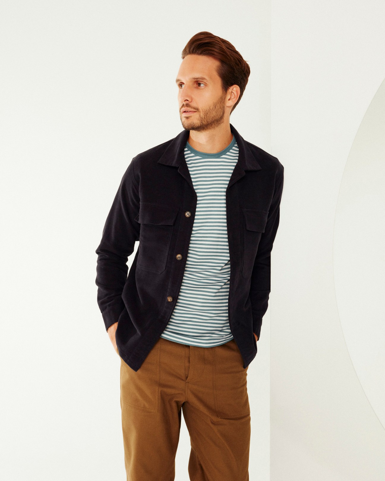 Man wearing navy corduroy blazer, striped shirt, and tan chinos against white background.