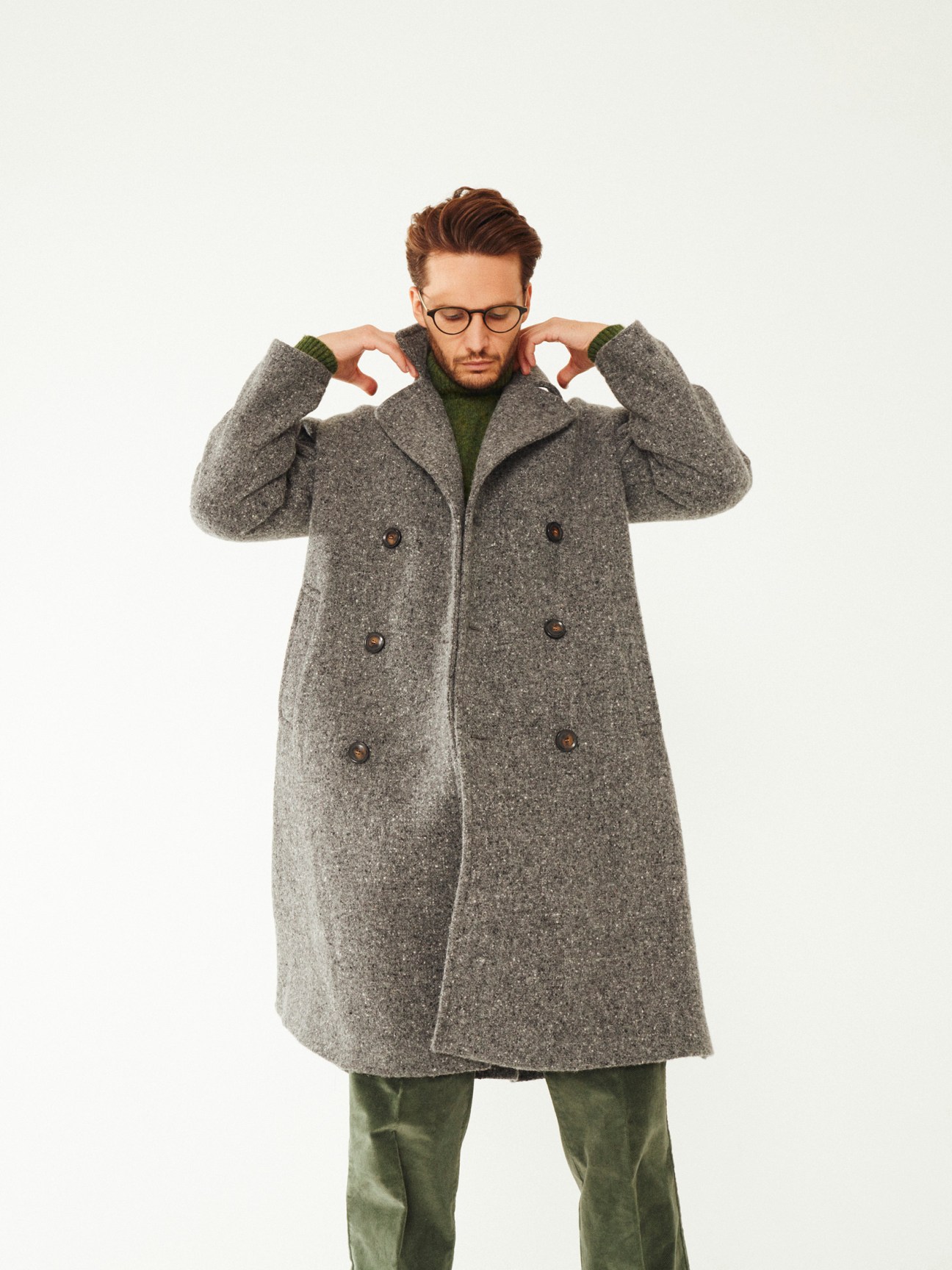 Man wearing gray wool coat and green turtleneck sweater with glasses