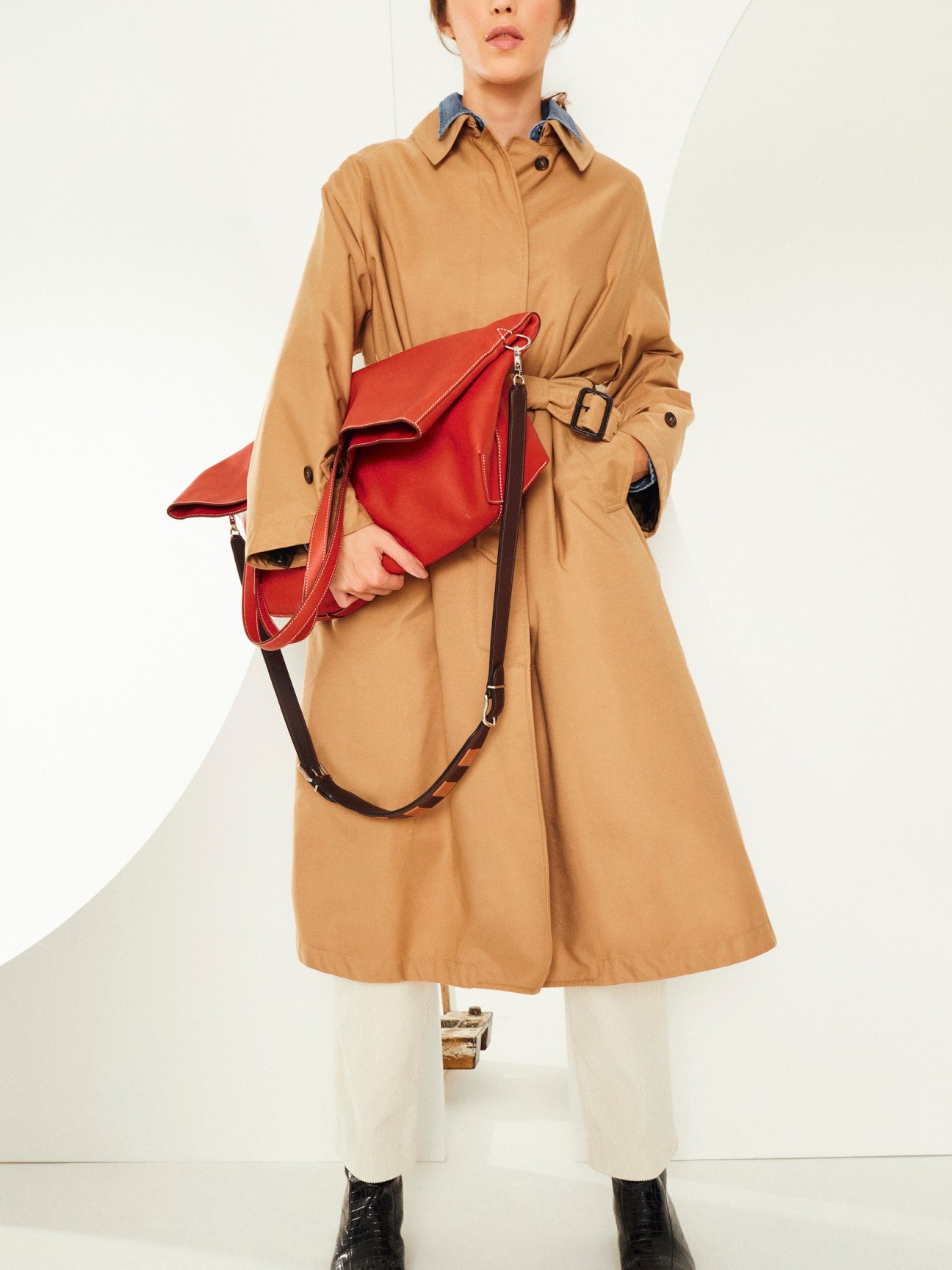 Woman wearing camel trench coat with red leather crossbody bag and black boots