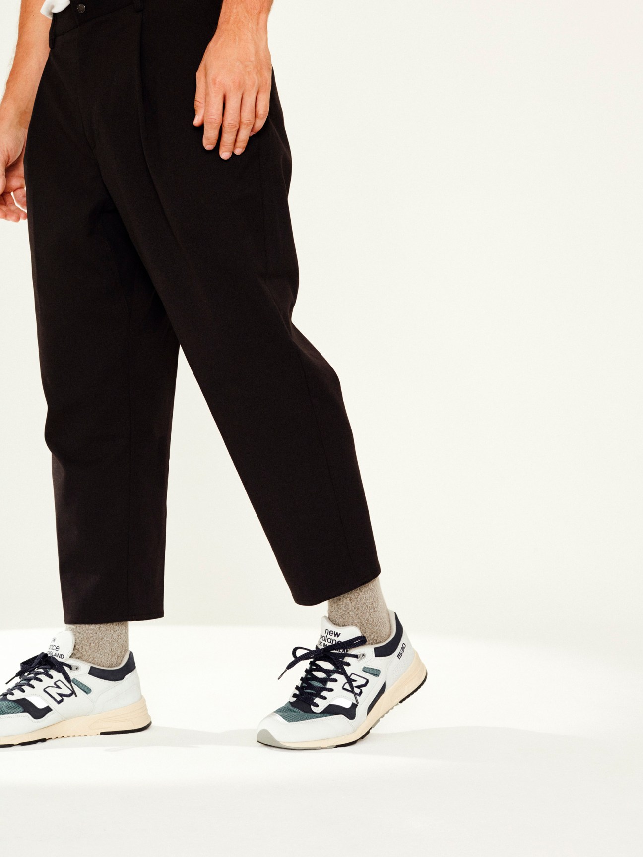Person wearing black cropped trousers, beige socks, and New Balance trainers with navy and cream colorway.