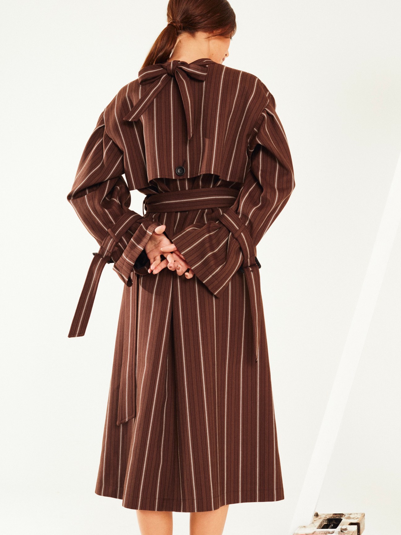 Woman wearing a brown pinstriped dress with a bow detail at the back, viewed from behind.