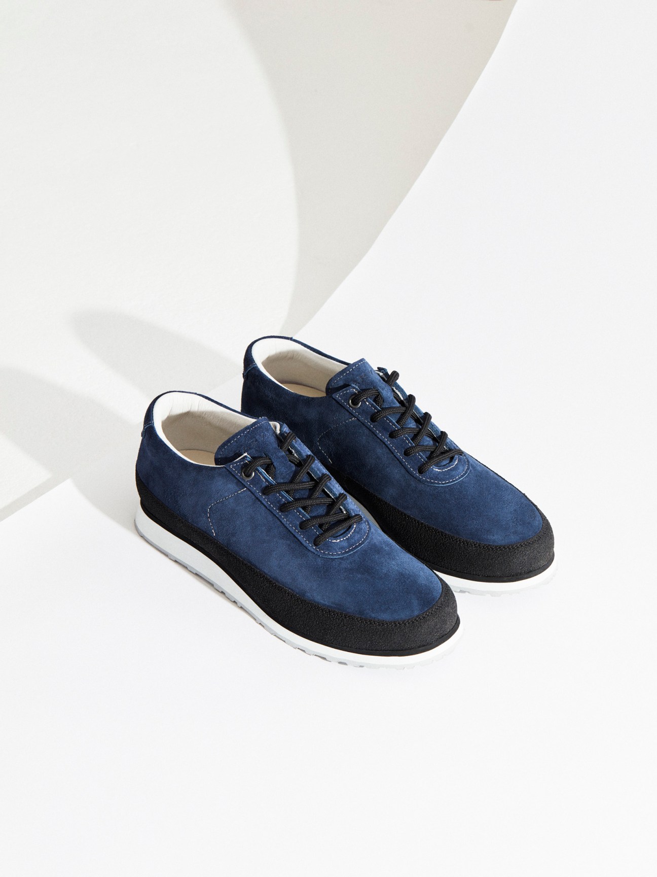 Pair of navy suede lace-up shoes with black rubber outsoles and white sock linings on white background.